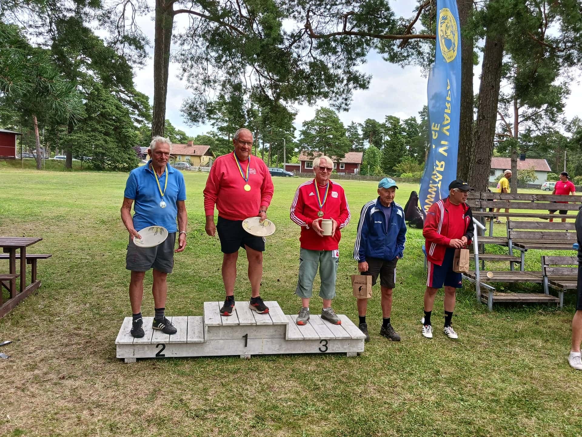 Oldboys på prispallen efter centimeter-finalen — fem veteraner med medaljer, varpor i händerna och förbundets blå banderoll i bakgrunden